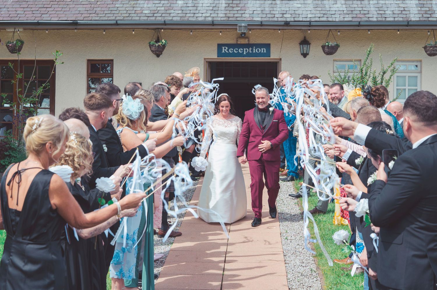 Newlywed couple exits reception venue through cheering guests waving ribbons in a joyful wedding send-off celebration.
