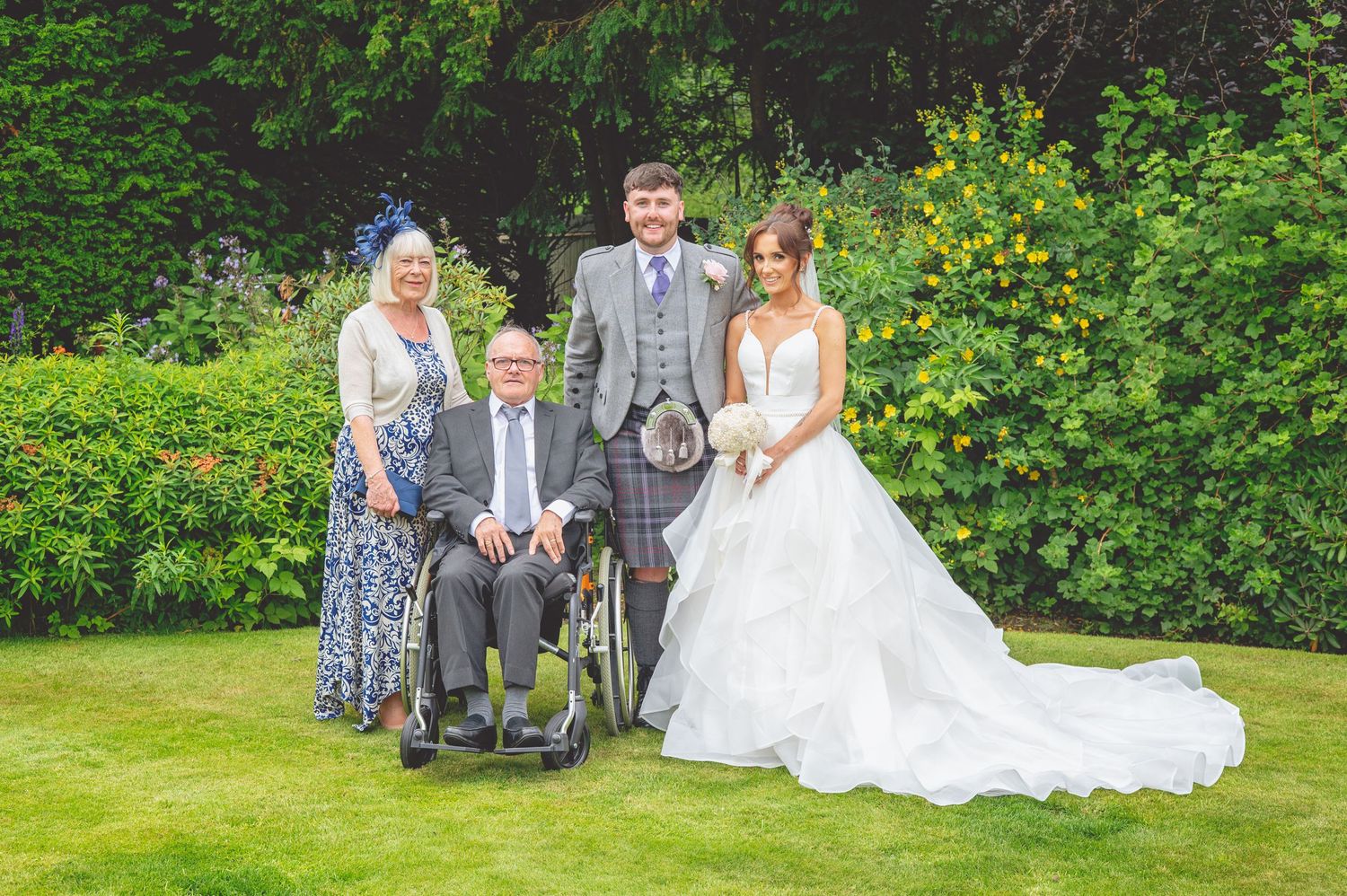 Wedding group photo with family members in formal attire on garden lawn.