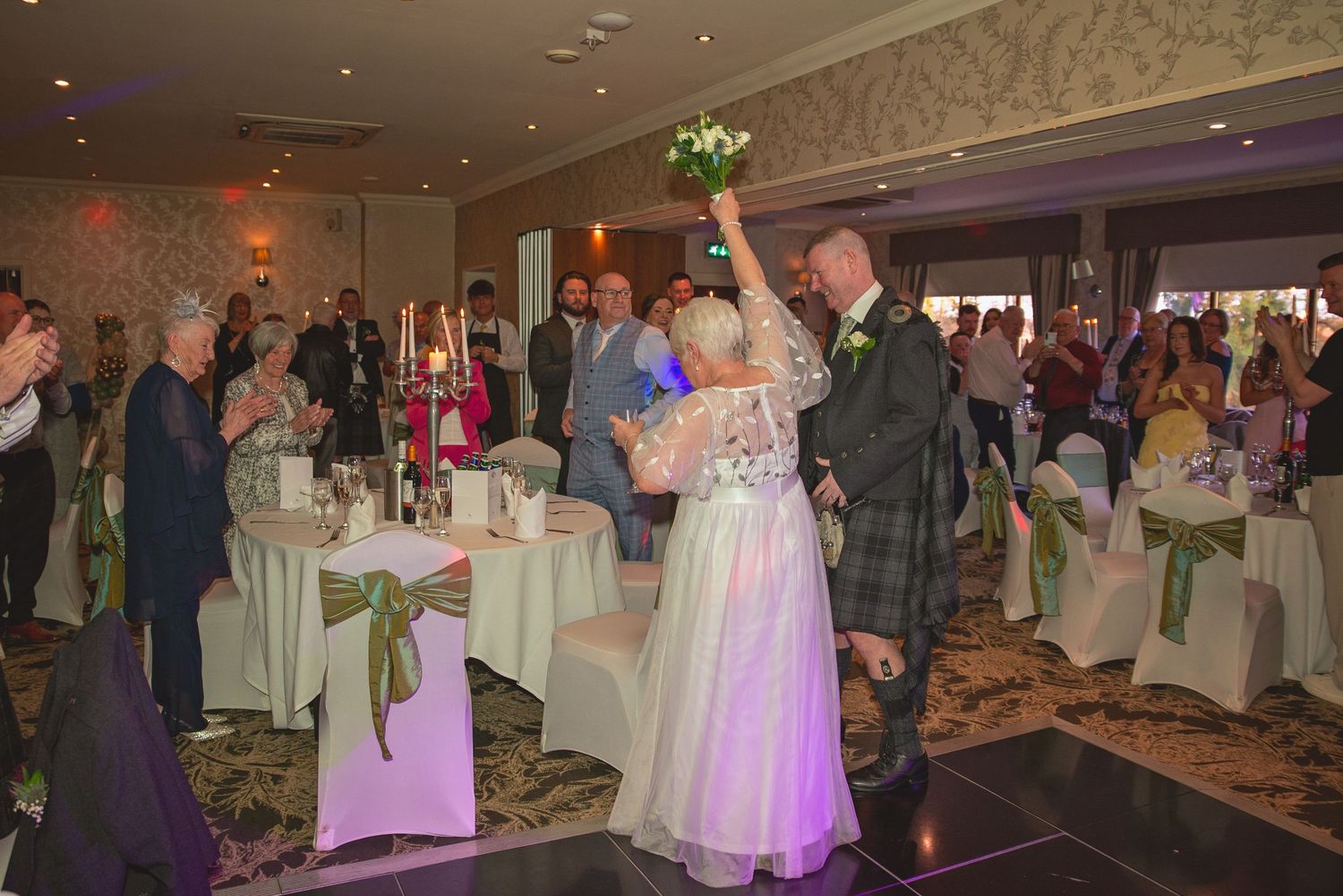 Wedding guests dancing and celebrating on a dimly lit dance floor at an evening reception.