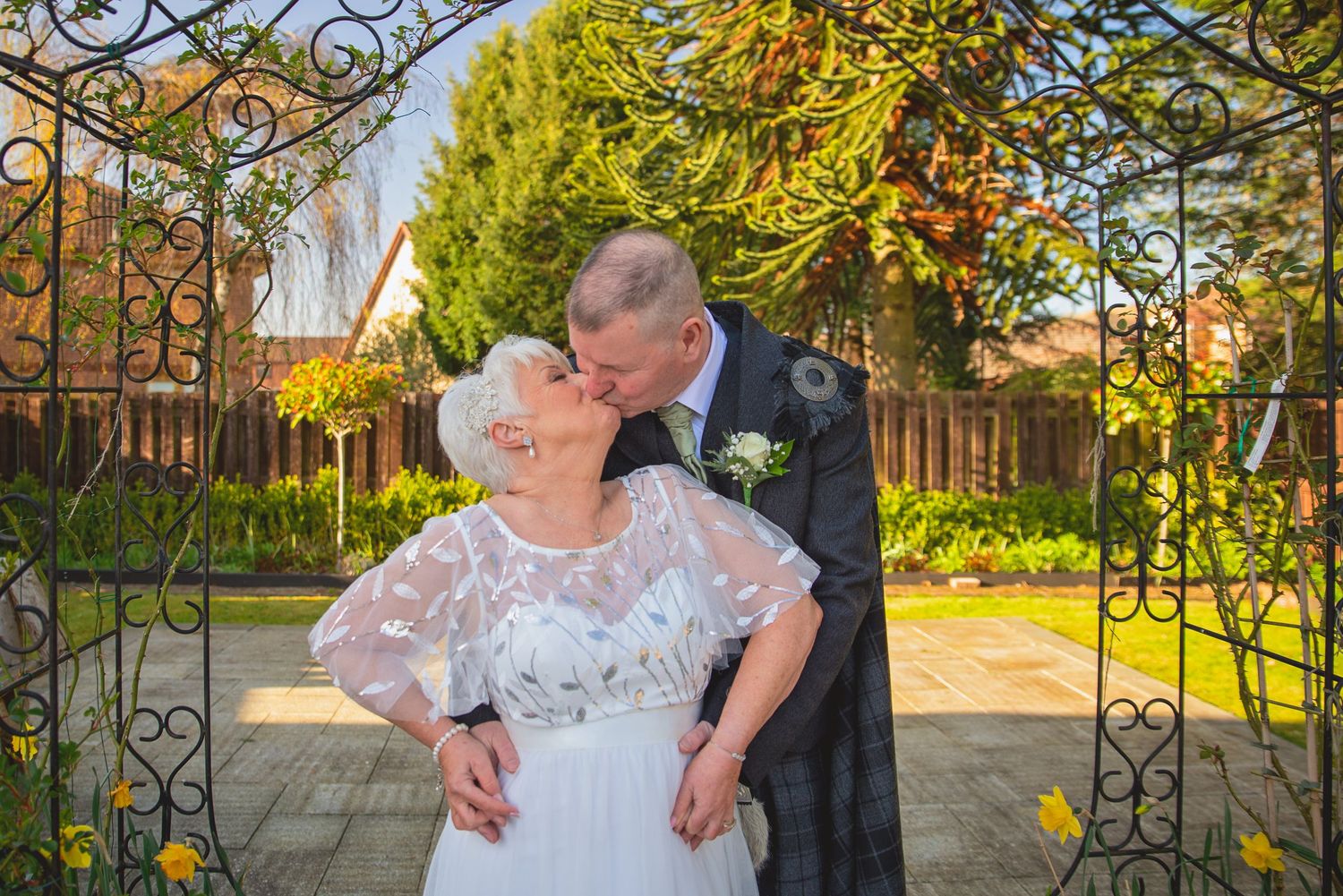 Scottish wedding couple embracing under an ornate garden archway during golden hour.