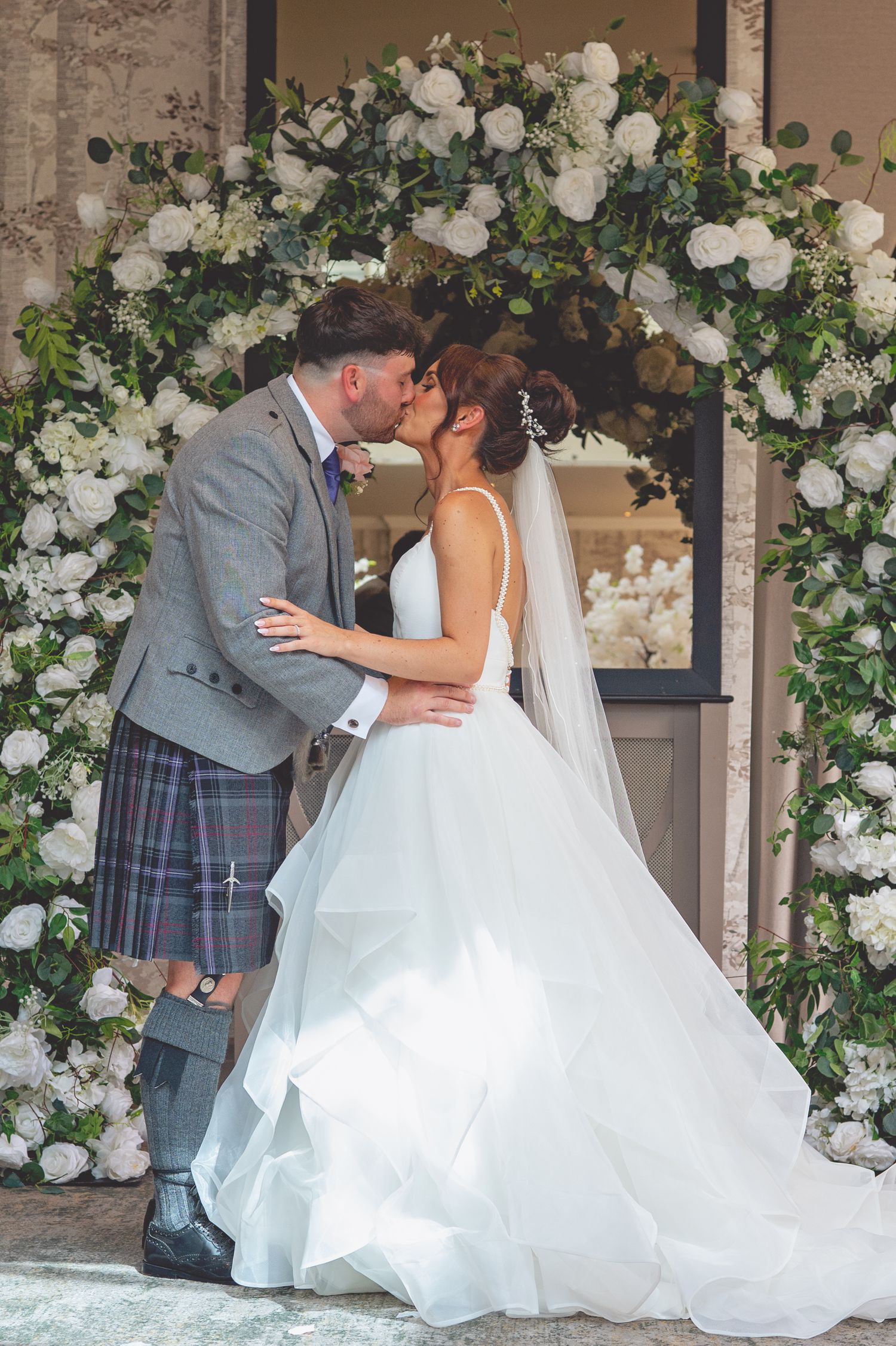 Newlyweds share romantic kisses against a backdrop of elegant white floral arrangements.