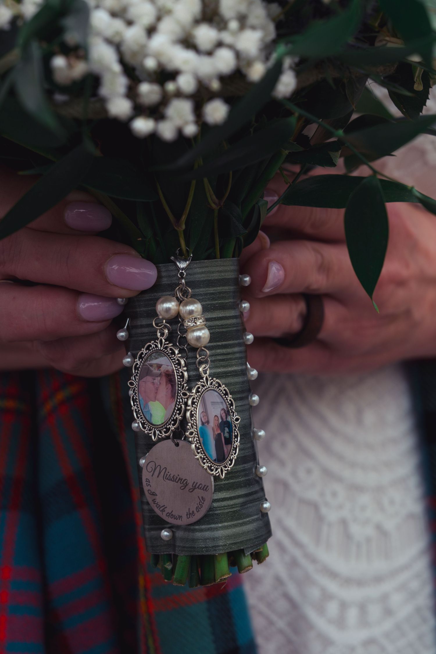 Bride holding floral bouquet with memorial photo charms and pearl accents, wearing pink nail polish at a wedding.