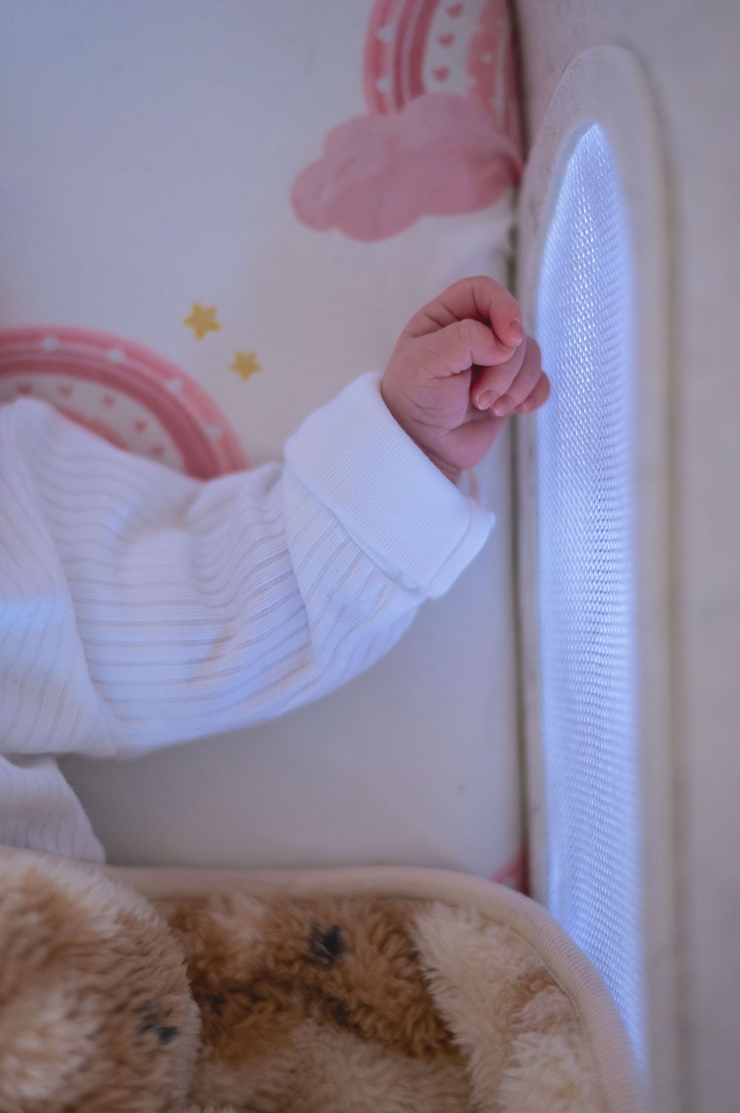 A white knit sweater sleeve reaching down against a soft pink background with window light.