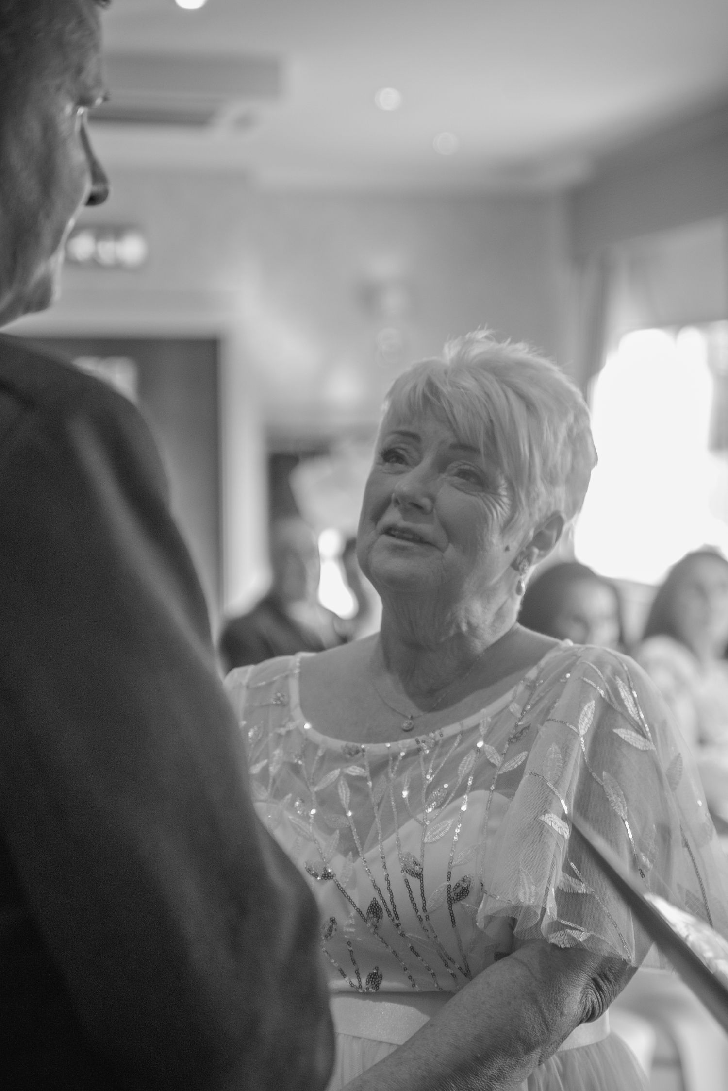 Black and white candid shot of wedding guest smiling during reception conversation.