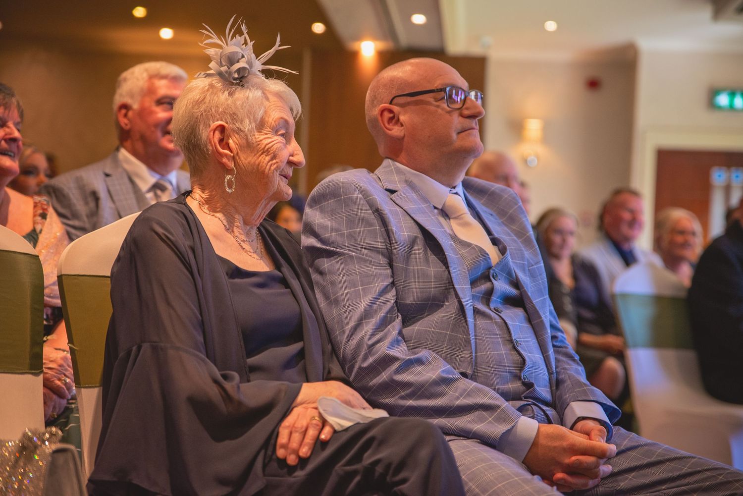 Wedding guests seated in rows during indoor ceremony.