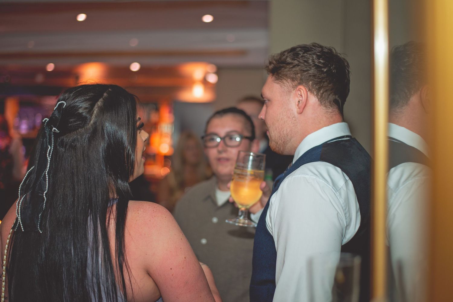 Wedding reception guests engaged in conversation in dimly lit venue.