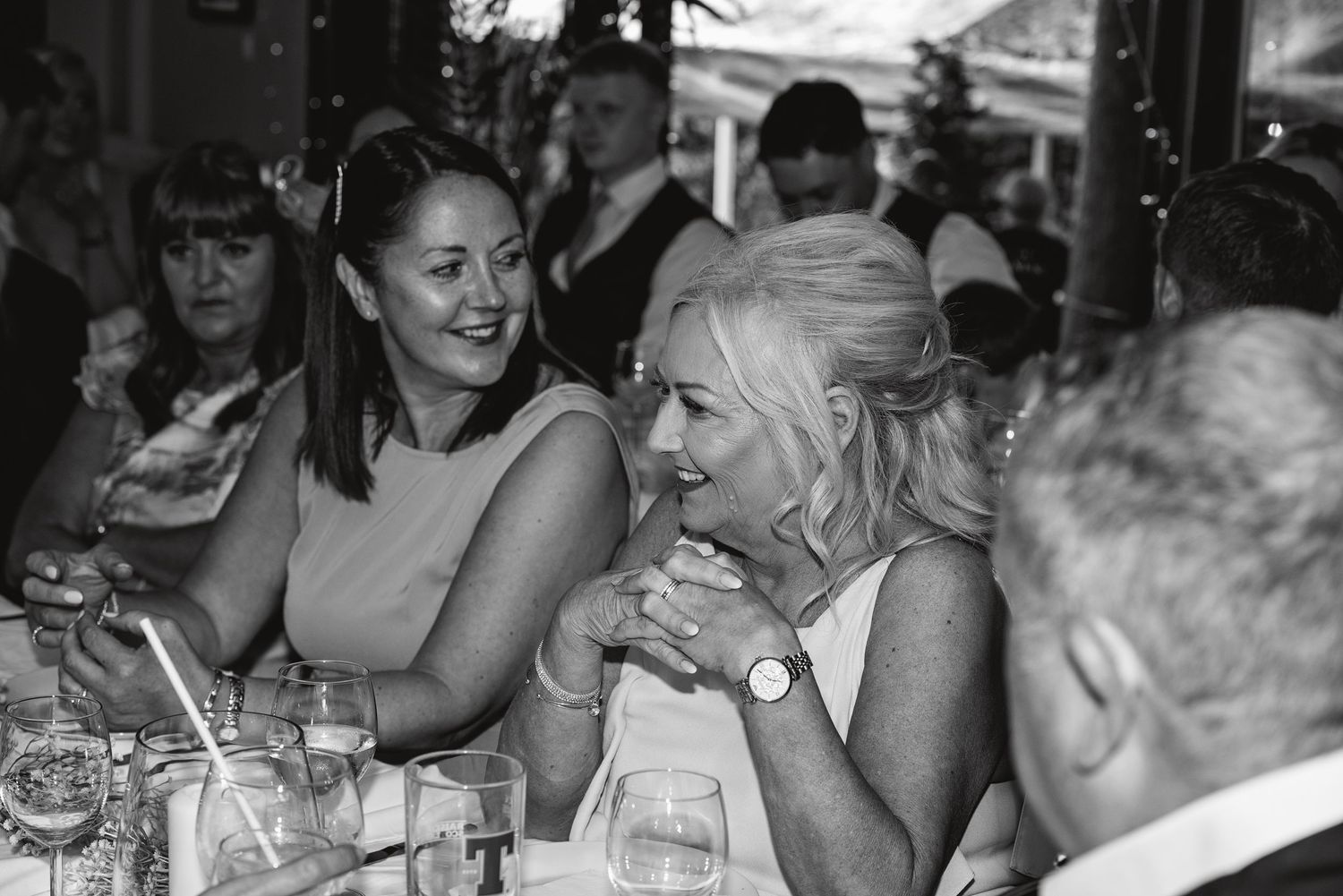 Black and white candid photo of wedding guests enjoying dinner at reception tables.