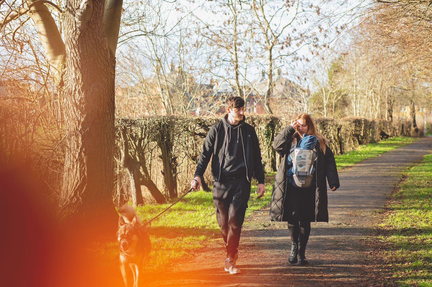 People walking along a tree-lined path on a sunny autumn afternoon with long shadows cast across the ground.