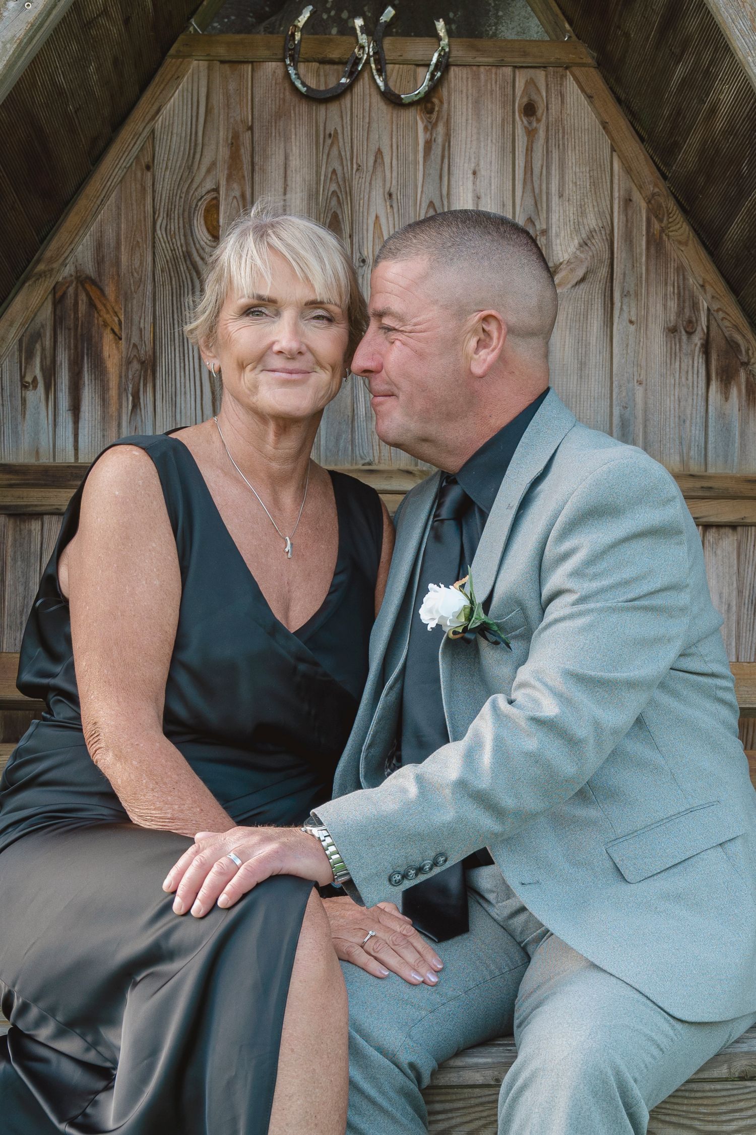 Elegant mature couple posing together at a wedding, woman in black dress, man in gray suit with boutonniere.