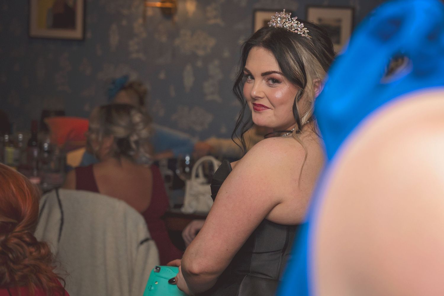 A young woman wearing a tiara and black dress smiles at a formal evening celebration event.