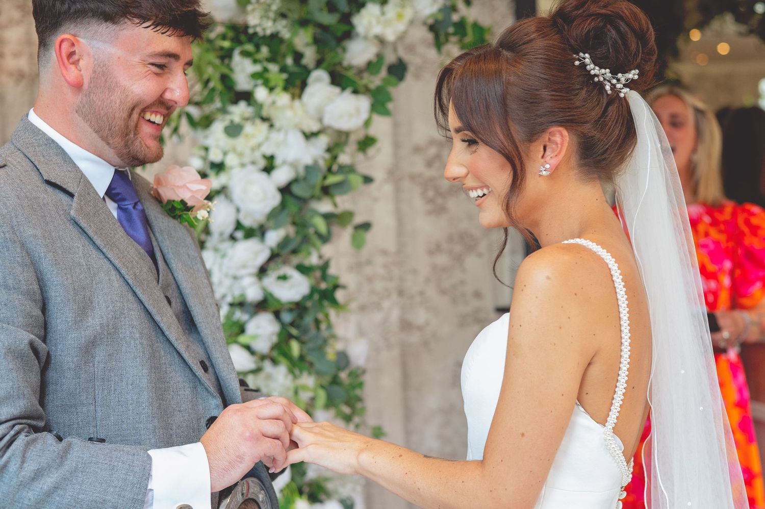 A couple shares a joyful moment during their ring exchange at an indoor wedding ceremony.