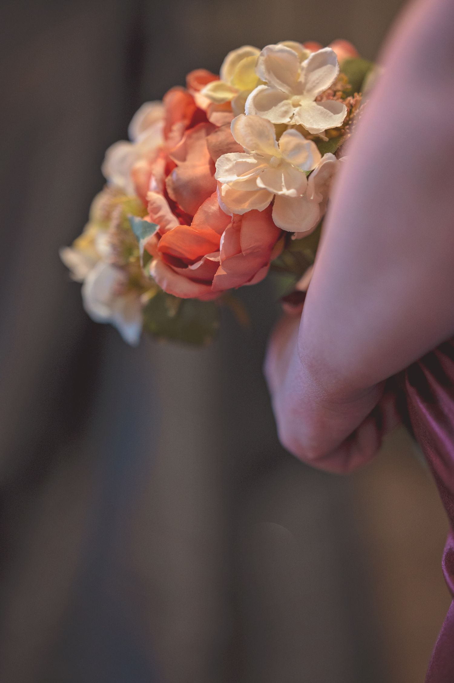 Close-up of elegant bridal wrist corsage with coral roses and cream hydrangeas on pink dress.