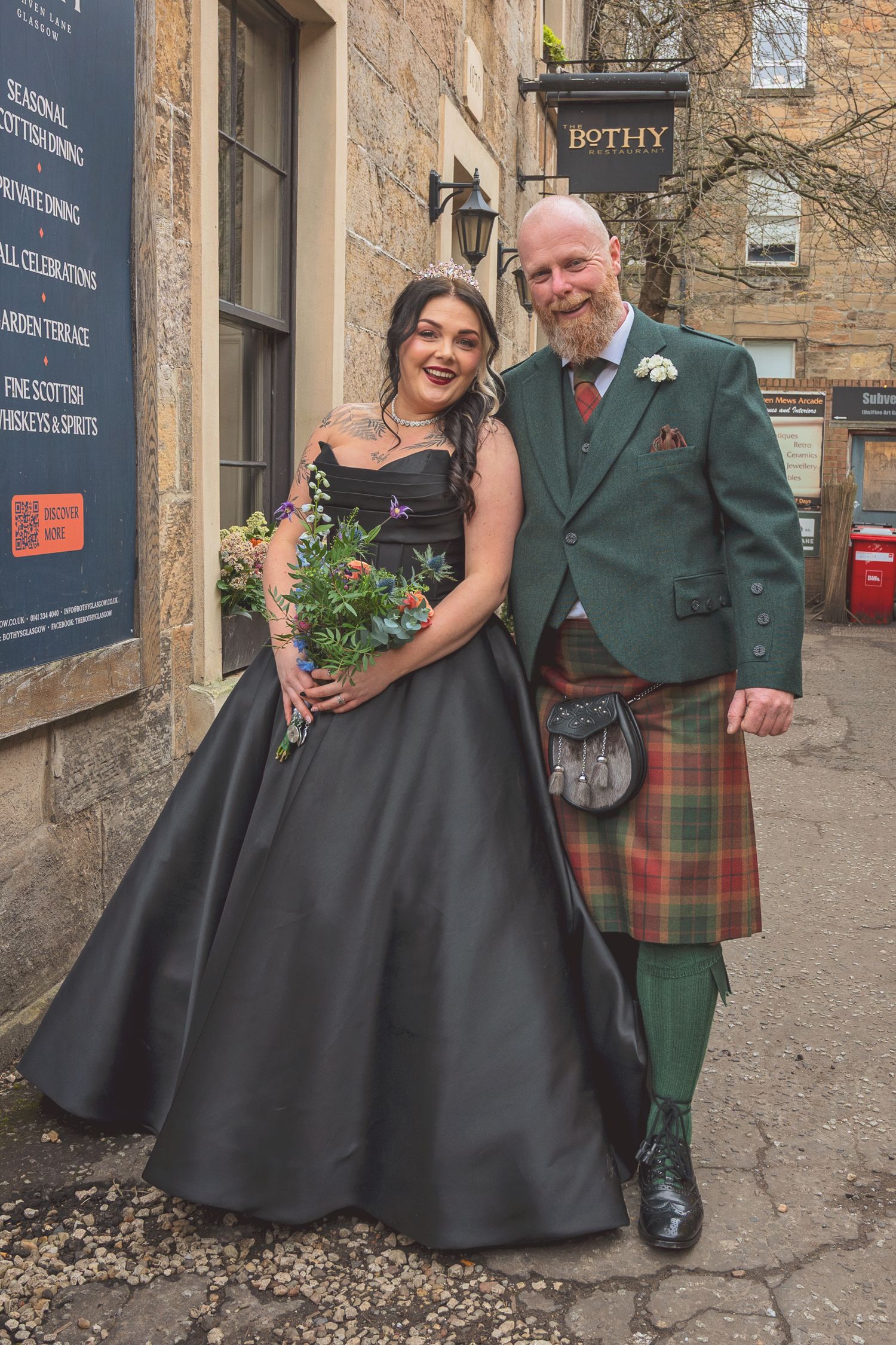 Bride in black gown with groom in green Scottish kilt outside The Bothy.
