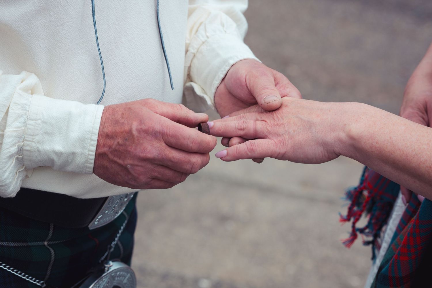 Man in Scottish kilt placing a ring on a woman's finger during a traditional wedding ceremony outdoors.
