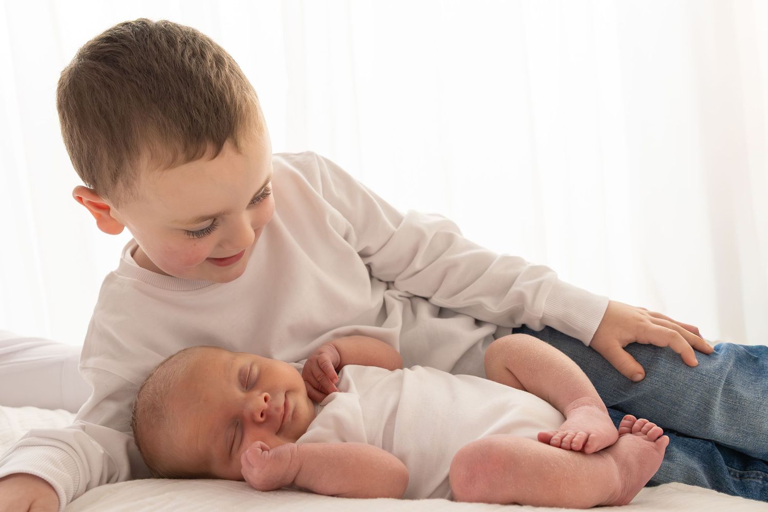 Little boy lying behind newborn baby brother, who is smiling., during a natural newborn photography session Wicklow