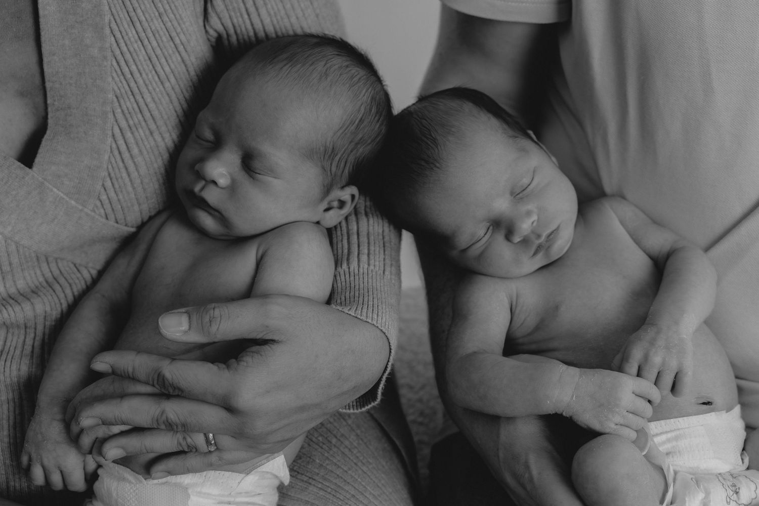 Twin babies asleep in their parents' arms, head to head during a natural newborn photography session Wicklow