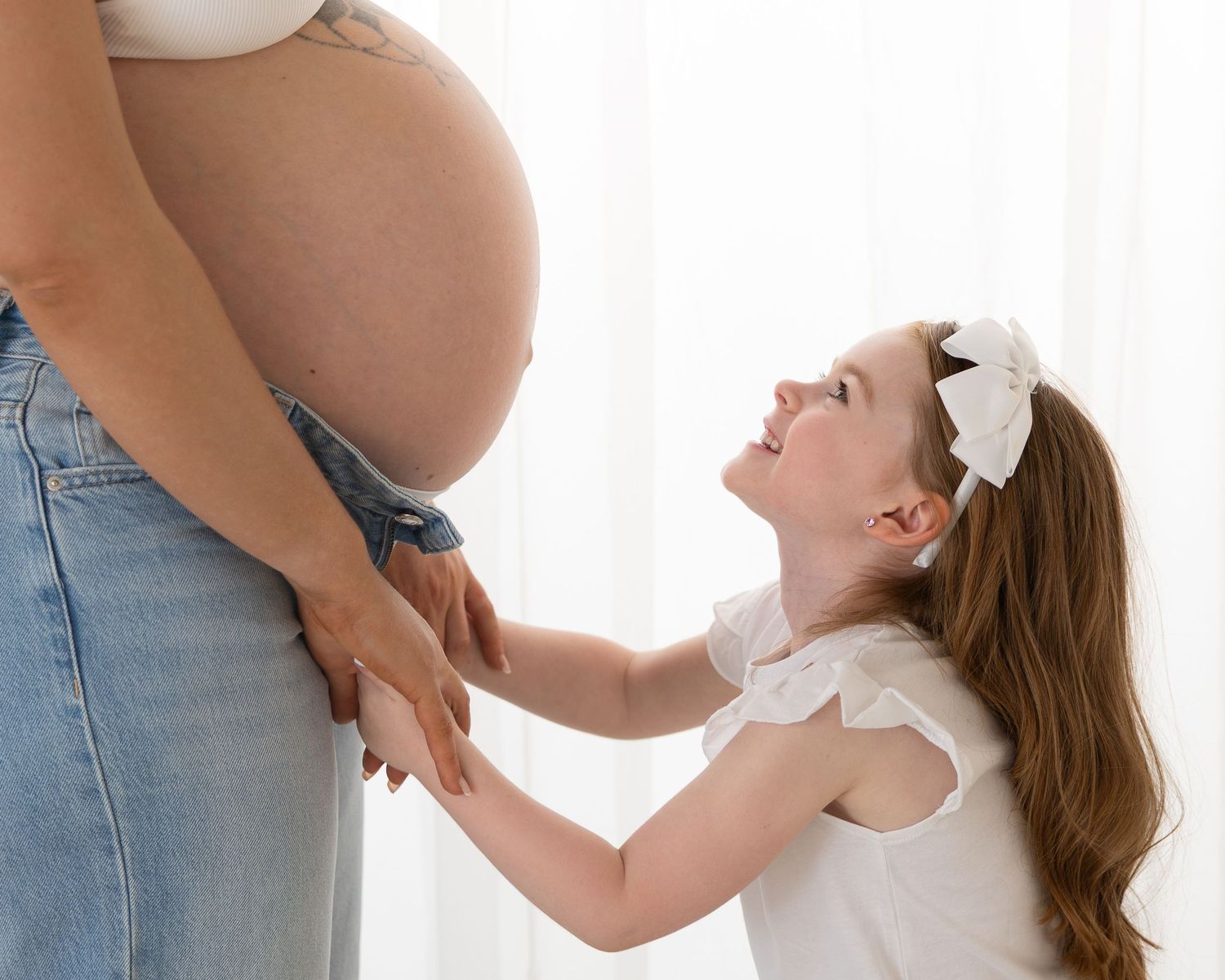 Little girl holding her mother's hands and looking up at her baby bump during a natural maternity photography Wicklow