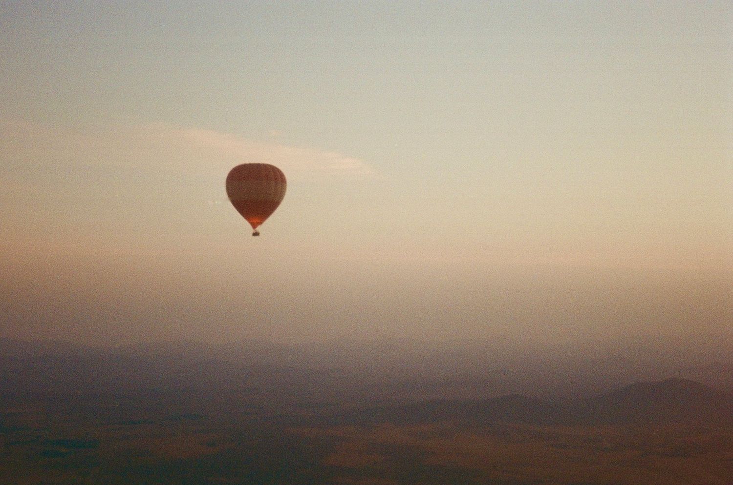 Cinematic travel film photograph of hot air balloons over Marrakech, Morocco at sunrise.
