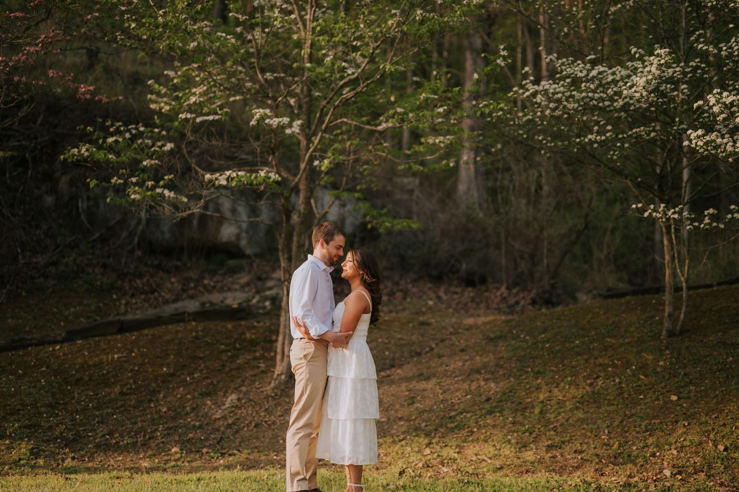 A romantic couple embraces on a wooded path during a golden sunset.