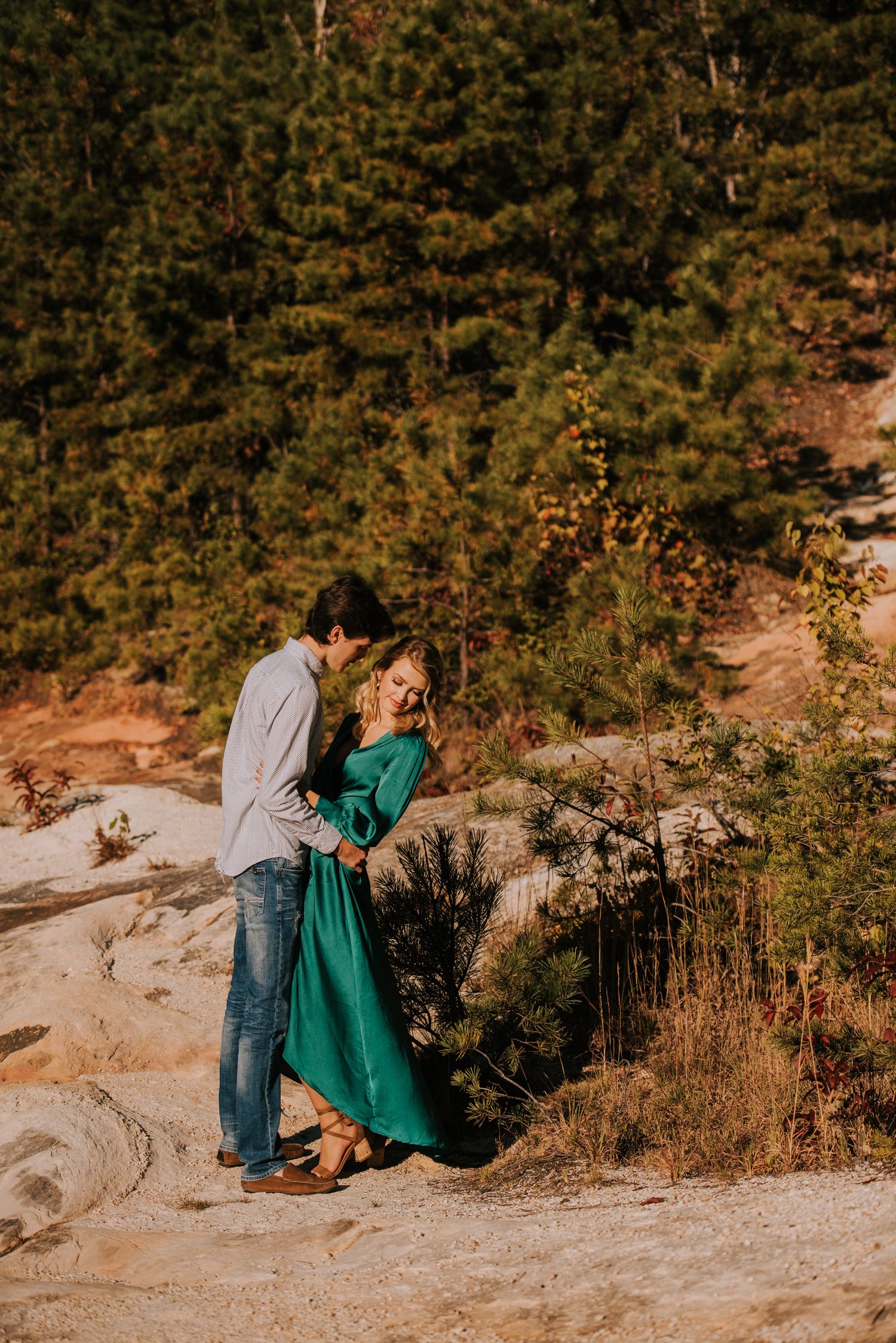 Romantic outdoor photoshoot on rocky terrain with green dress and casual attire.