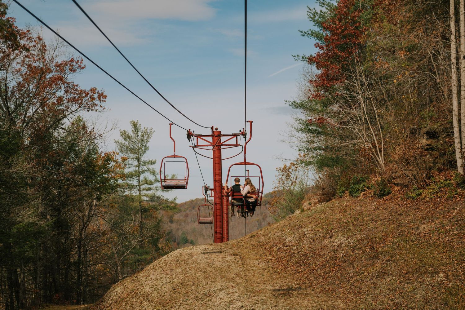 Red ski lift chairs against blue sky with autumn trees in the background.