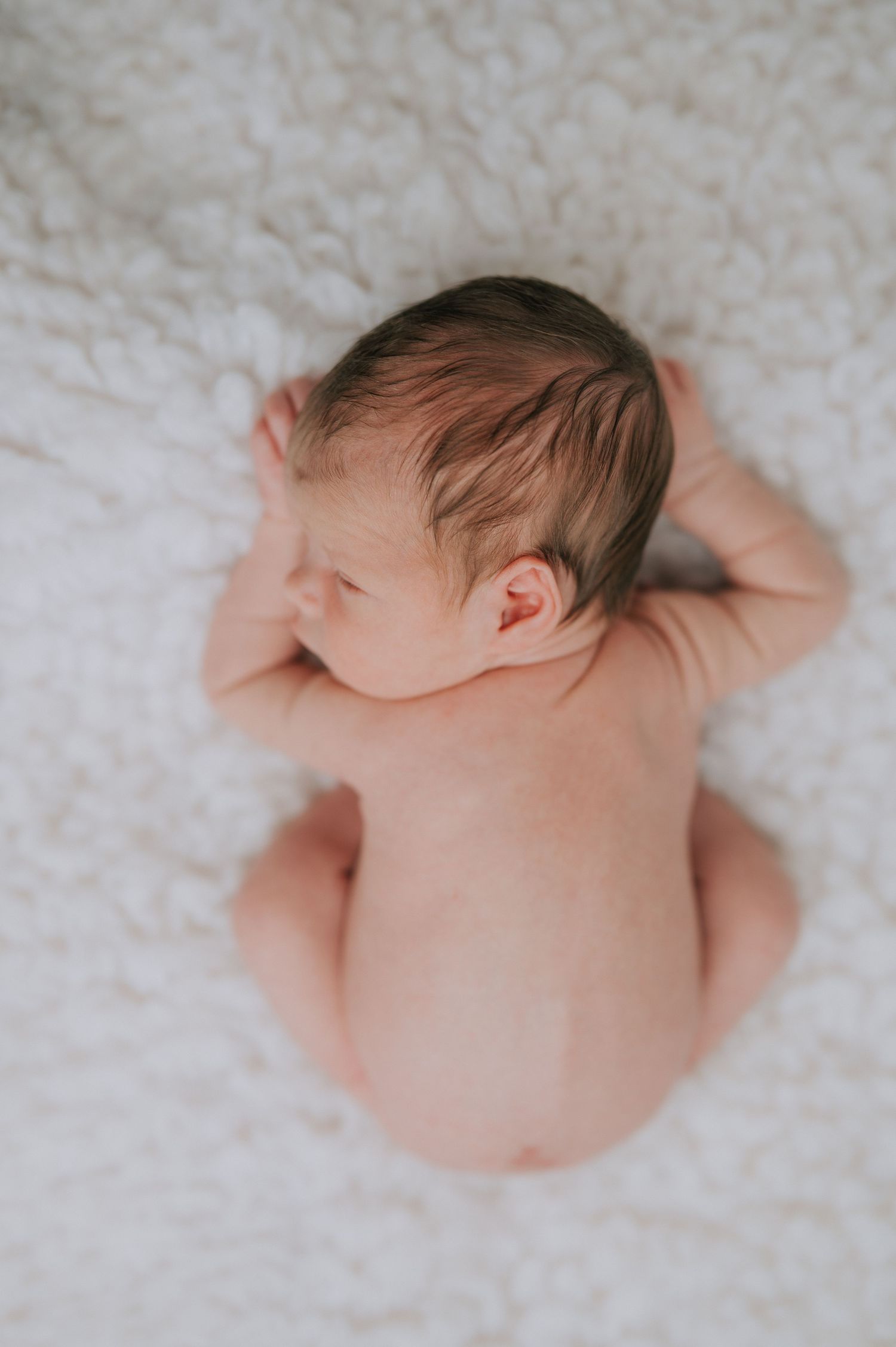 Overhead view of a sleeping newborn baby lying on soft white textured fabric.