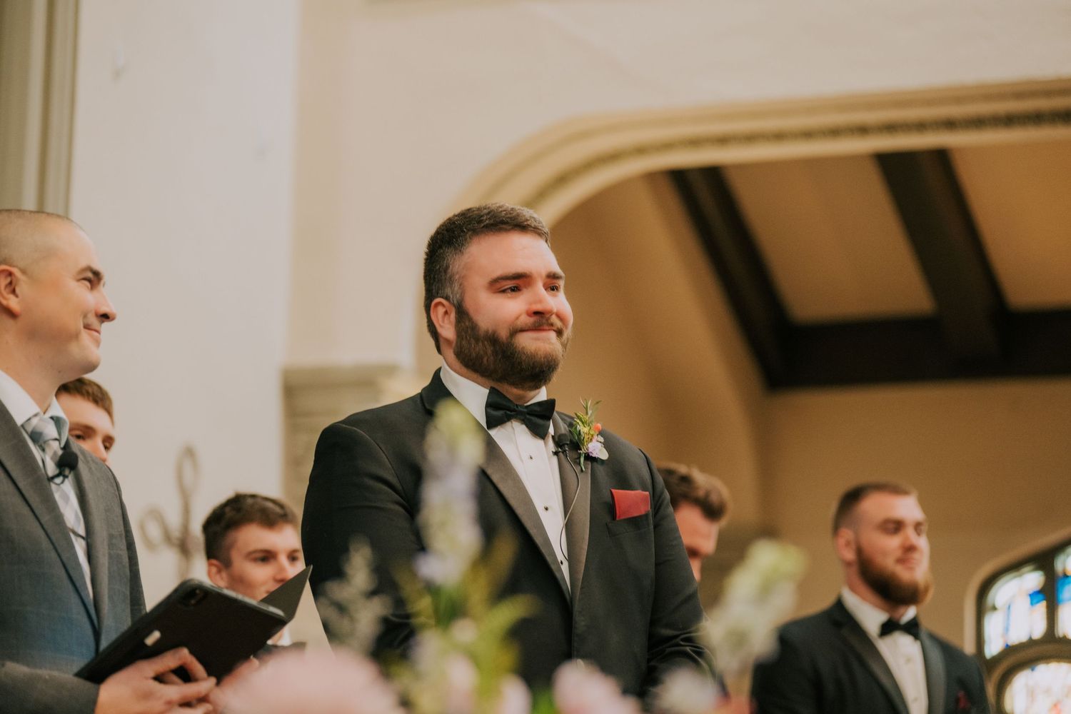 A groom and his groomsmen stand at the altar during an indoor wedding ceremony.