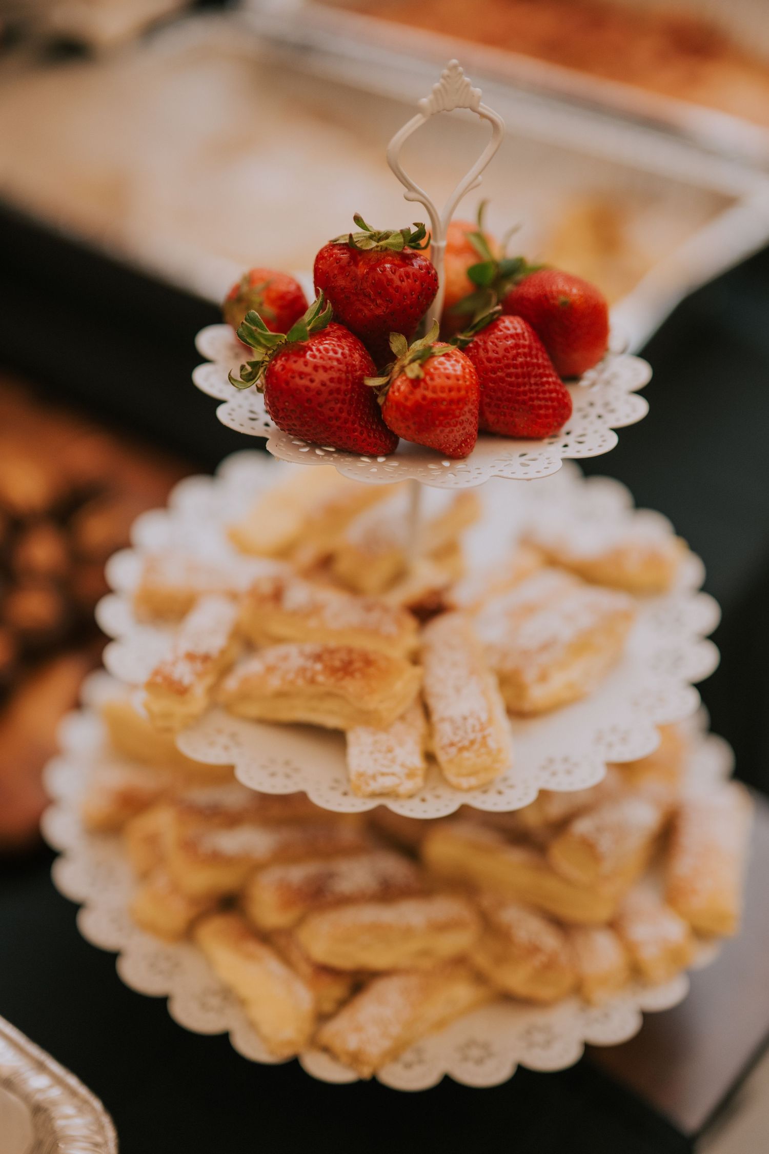 Three-tiered white dessert stand holds fresh strawberries on top and golden pastries on lower tiers.