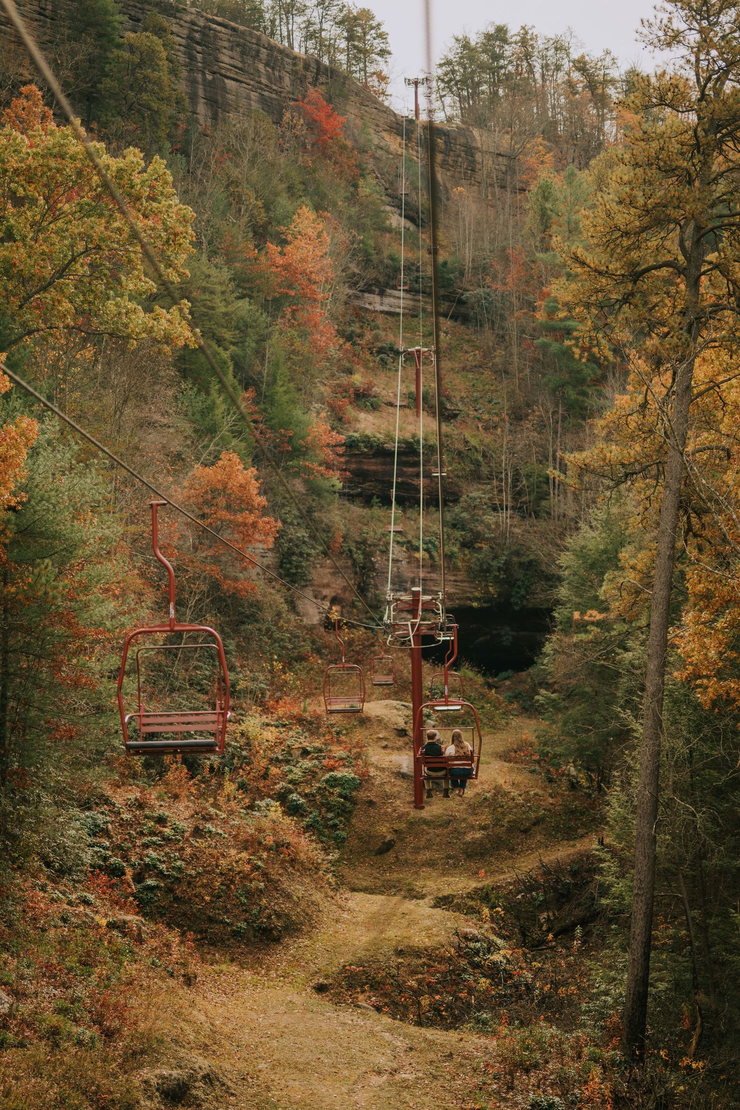 Empty ski lifts traverse through a forest landscape covered in fall colors.