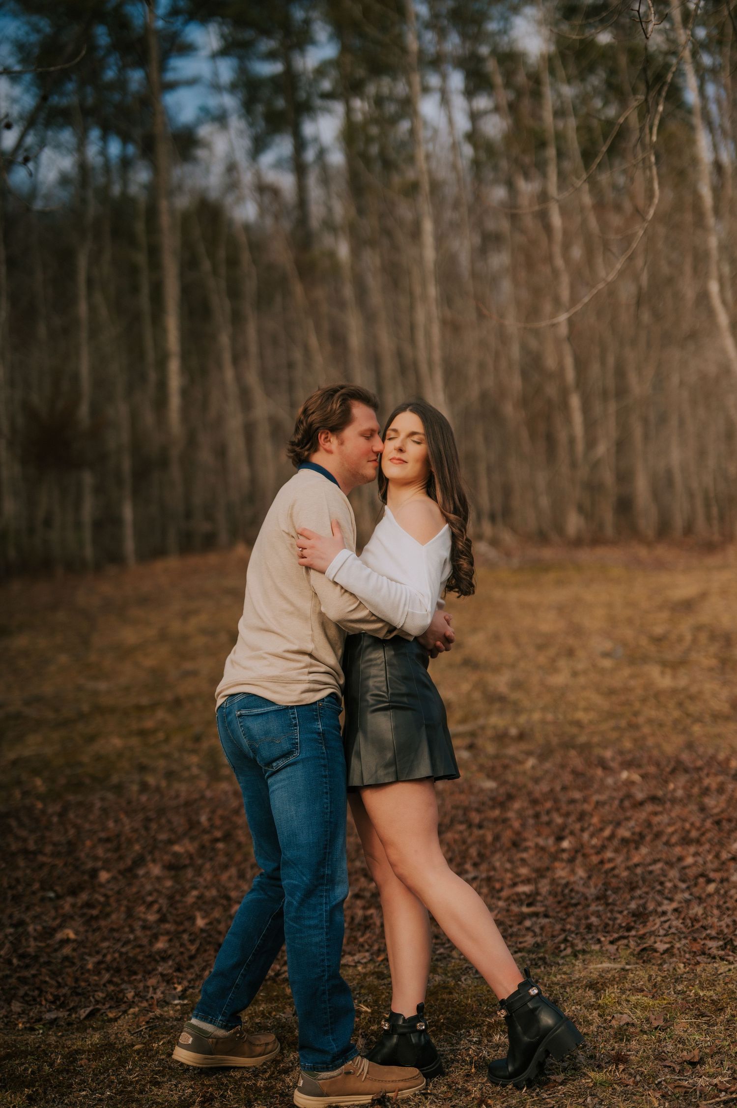 Autumn engagement photos in a wooded setting with fallen leaves.