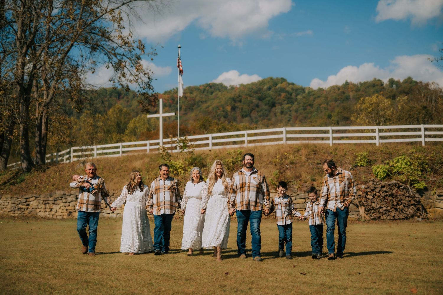 Wedding party poses in line against rustic fence and autumn landscape.