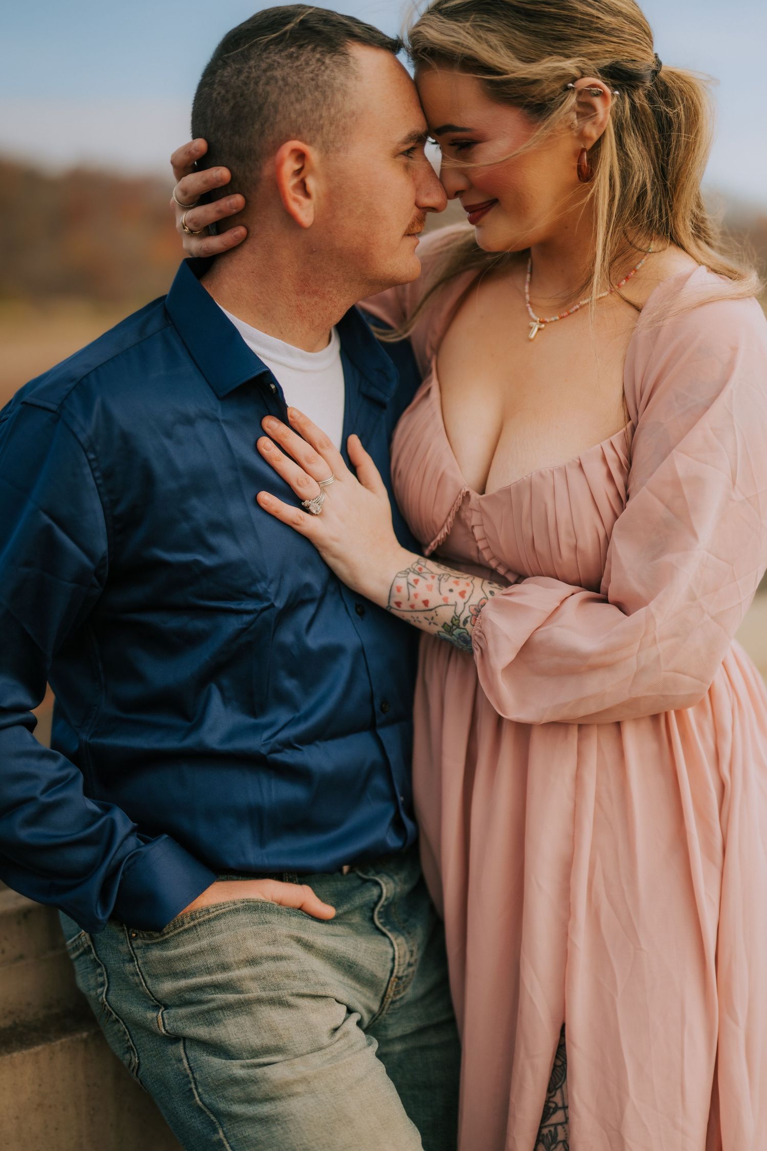 Tender moment between couple in pink dress and denim against natural outdoor backdrop.