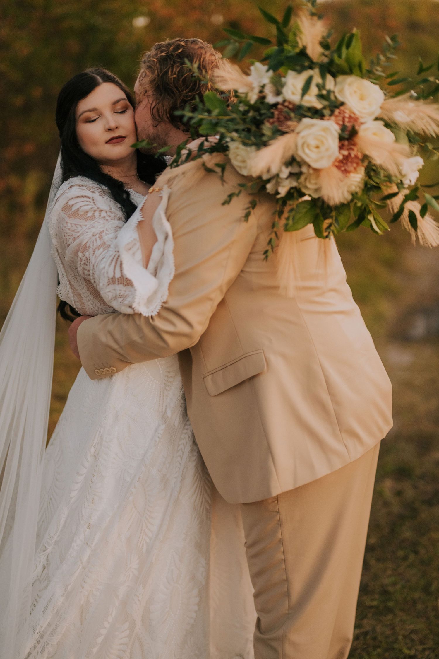 Intimate wedding couple embrace with floral bouquet and flowing white dress.