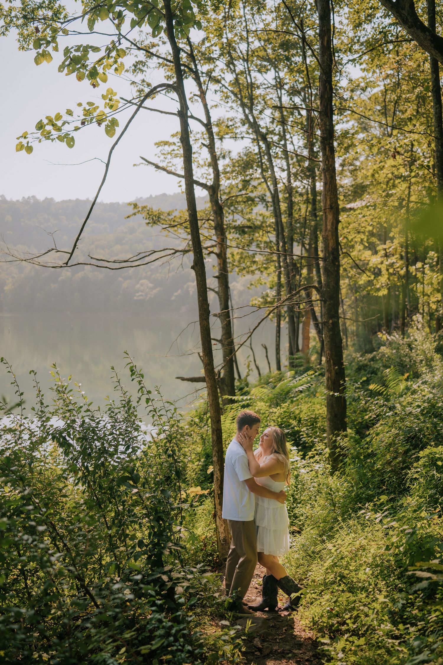 Couple standing together on wooded overlook with lake view in background.