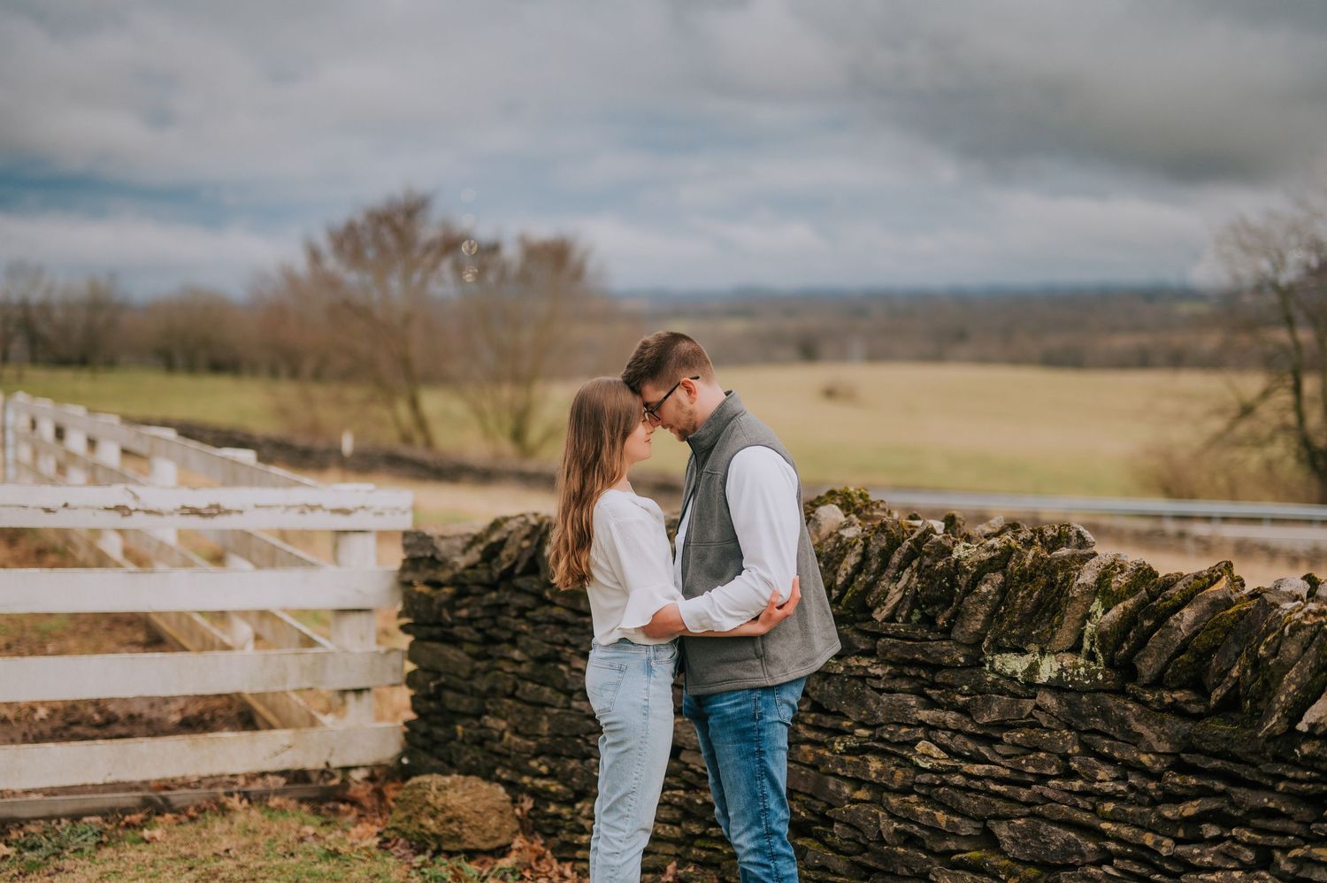 Stone wall and white fence stretching across rolling countryside landscape.