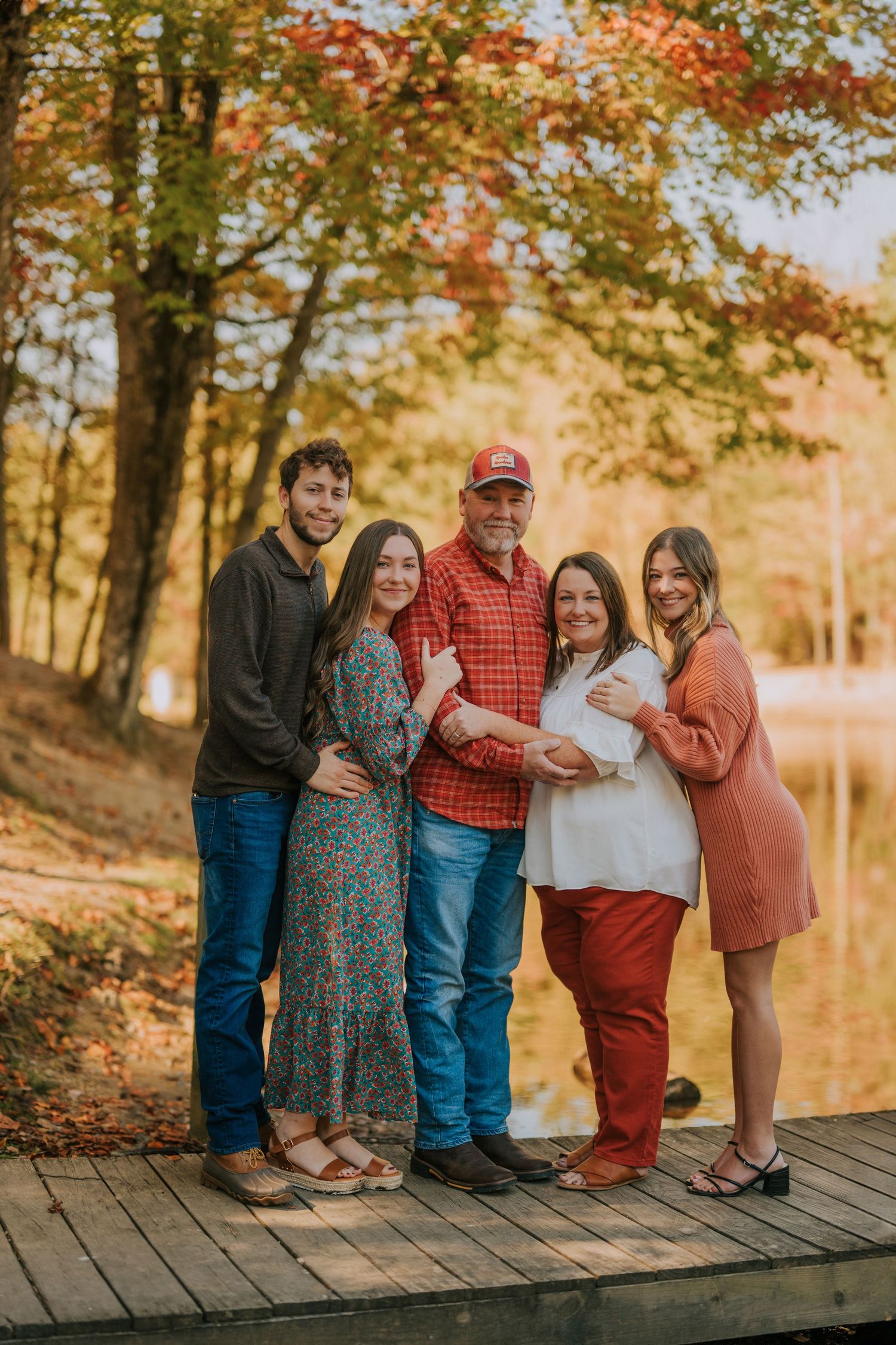 A group poses together on a wooden boardwalk during a fall photoshoot near a lake.