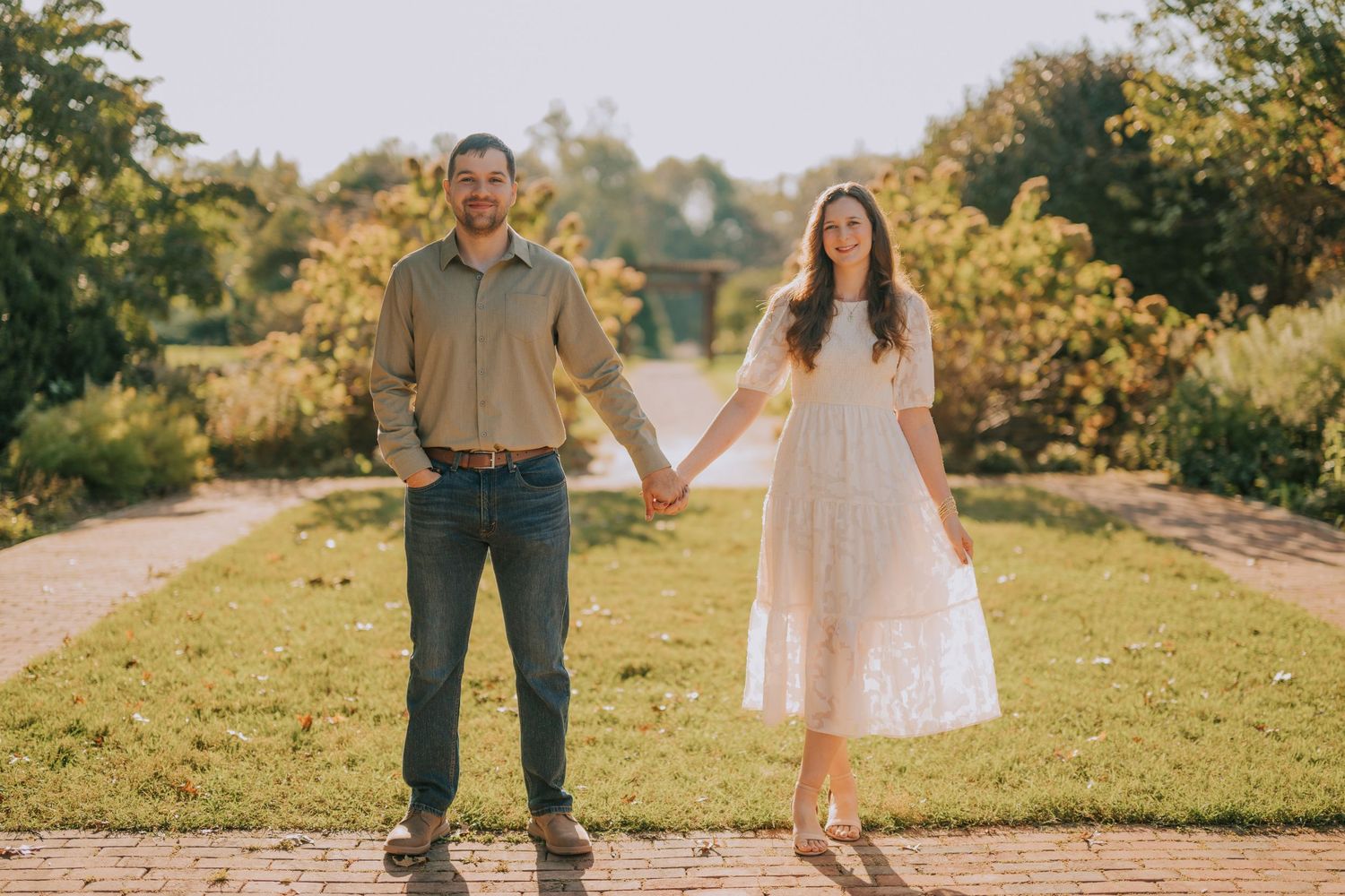 A couple shares joyful moments together on a sunlit path surrounded by greenery.