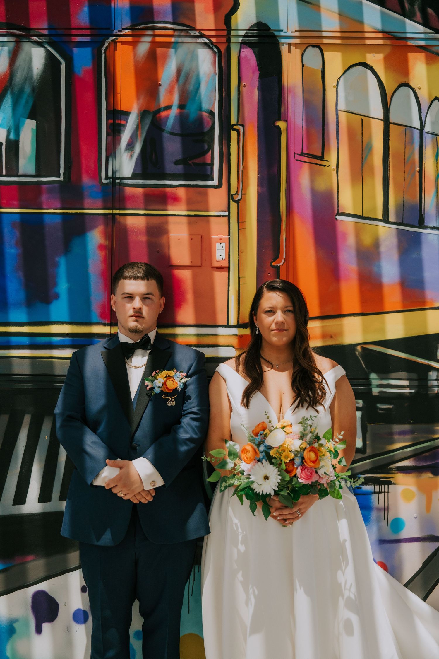 Wedding couple poses against vibrant graffiti wall with colorful street art backdrop in urban setting.