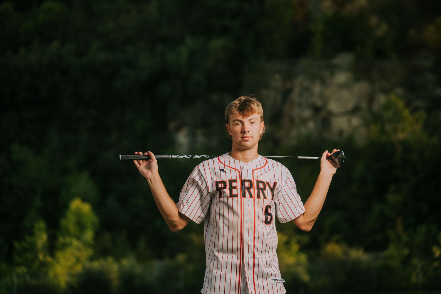 Baseball player in vintage striped uniform stands on field during golden hour photography session.