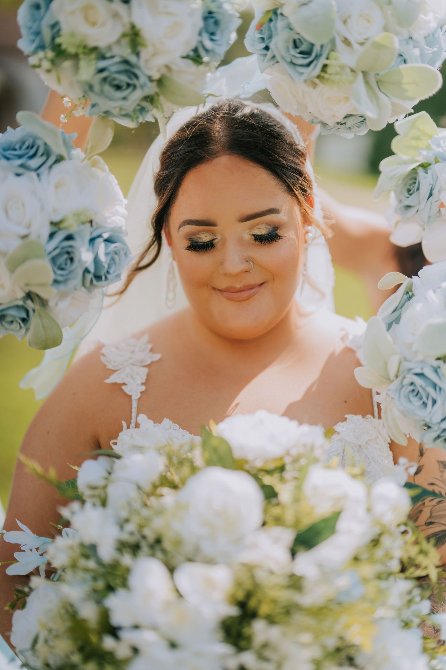 A bride smiles softly while surrounded by blue and white roses in a romantic wedding portrait.