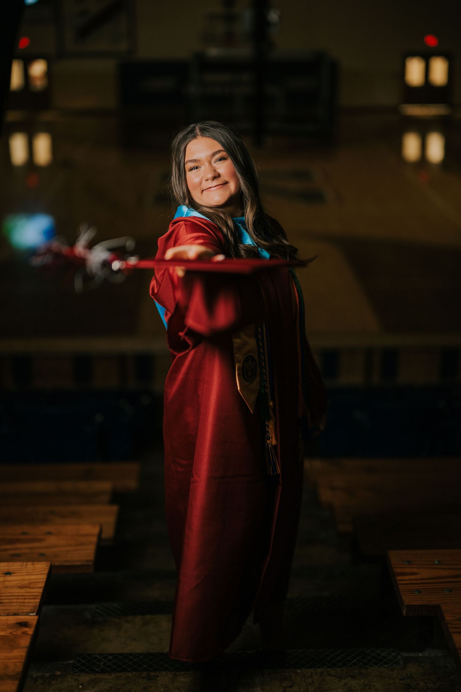 Graduate in red academic regalia posing in dimly lit indoor setting.