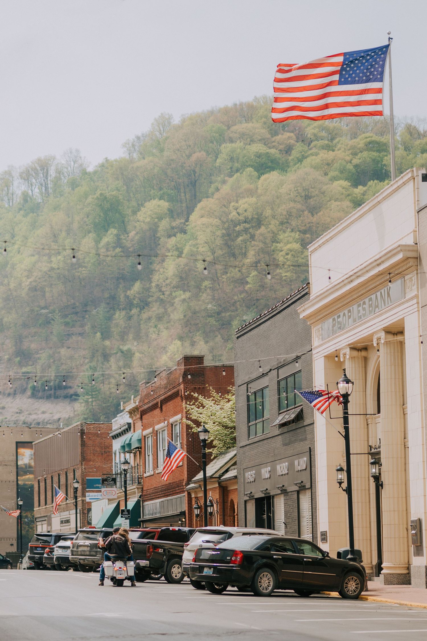 Small town main street with American flags and historic buildings against a hillside.