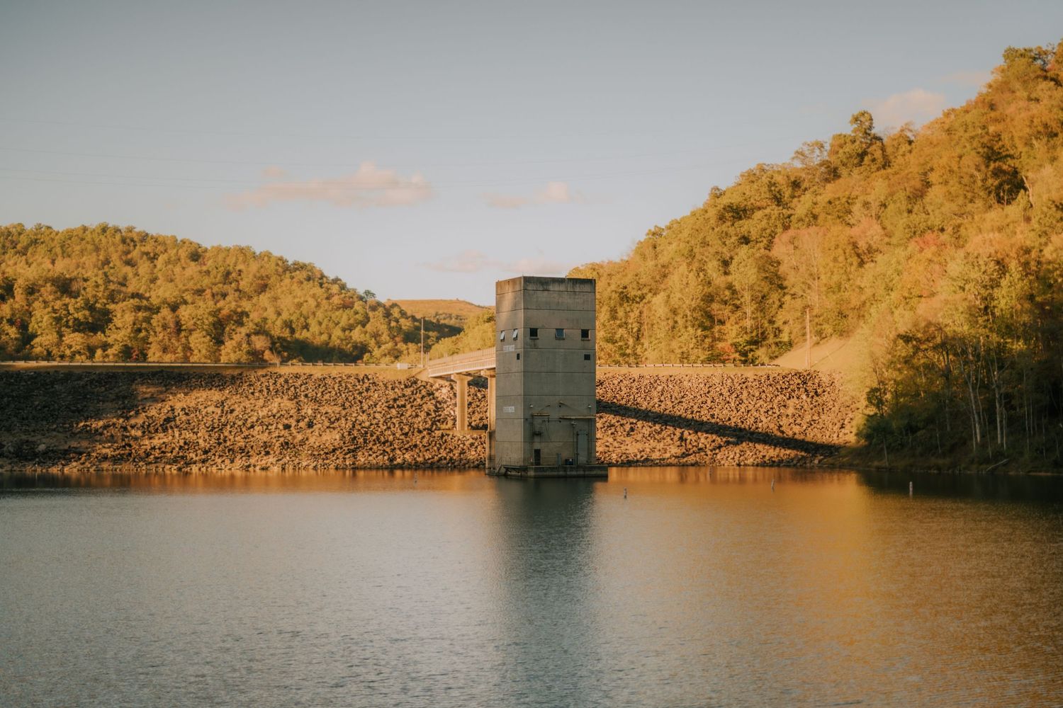 Golden sunset view of a dam and reservoir surrounded by autumn hills.