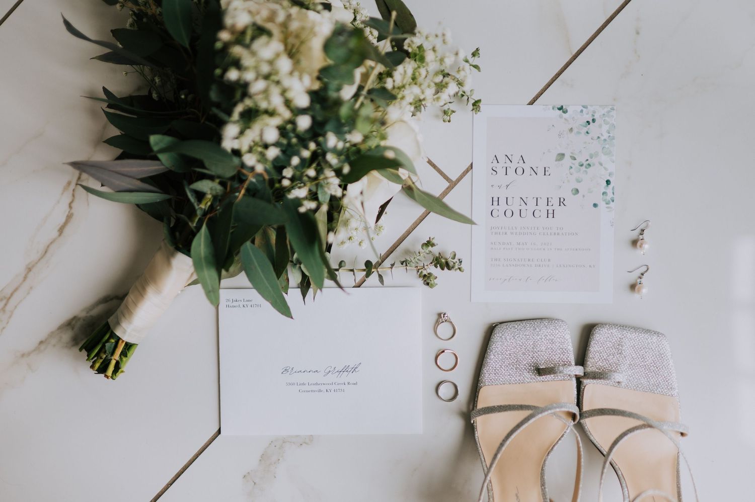 Wedding stationery and floral arrangements styled on white surface.