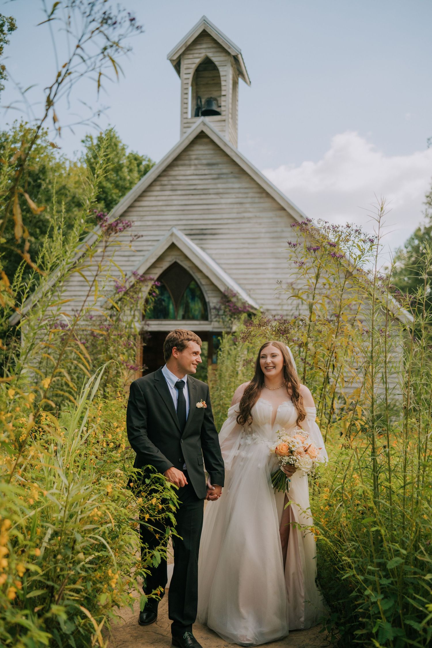 Small white chapel surrounded by tall wildflowers creates a romantic wedding backdrop.