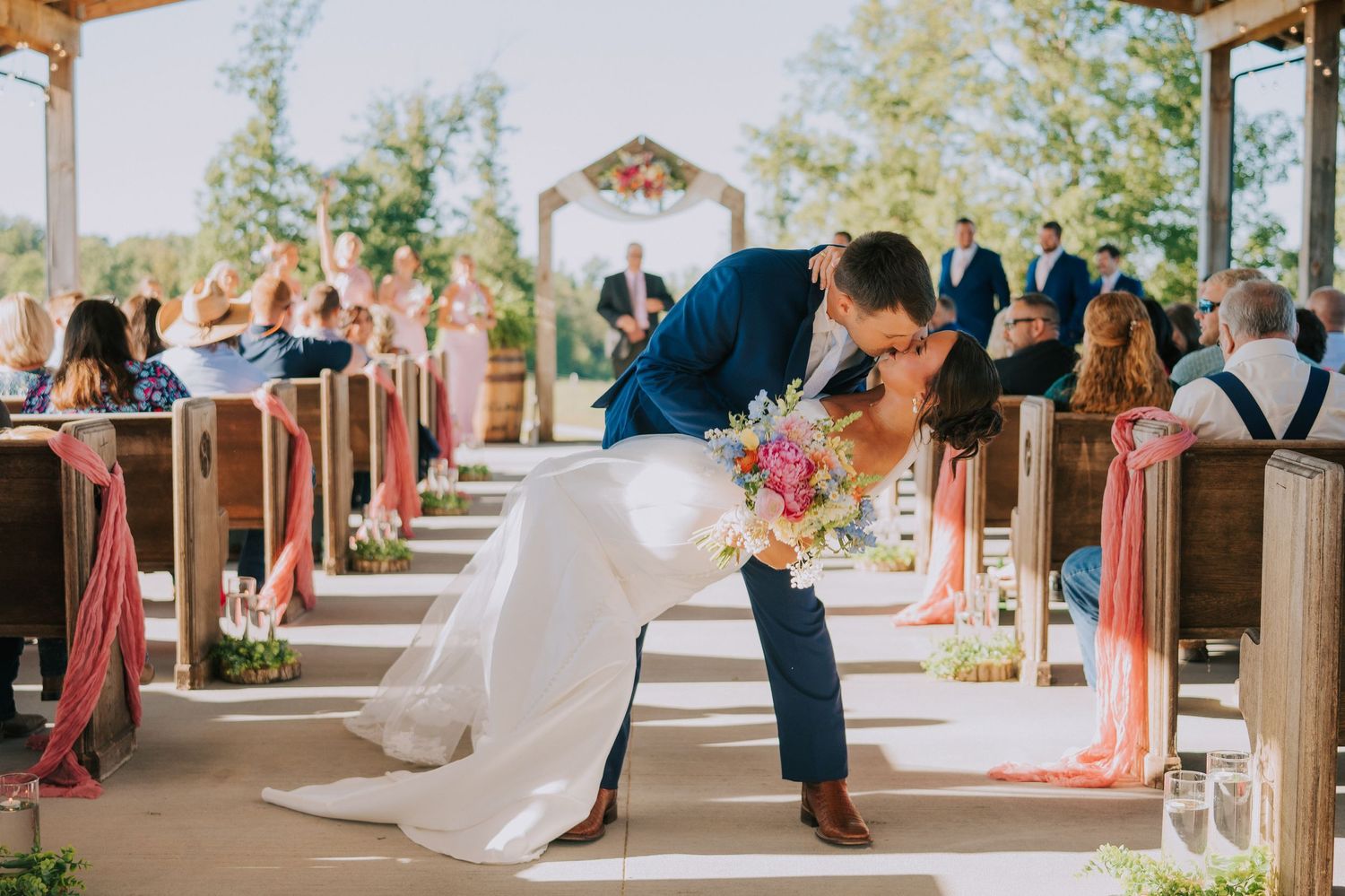Wedding ceremony setup in rustic outdoor venue with white decor and natural lighting.