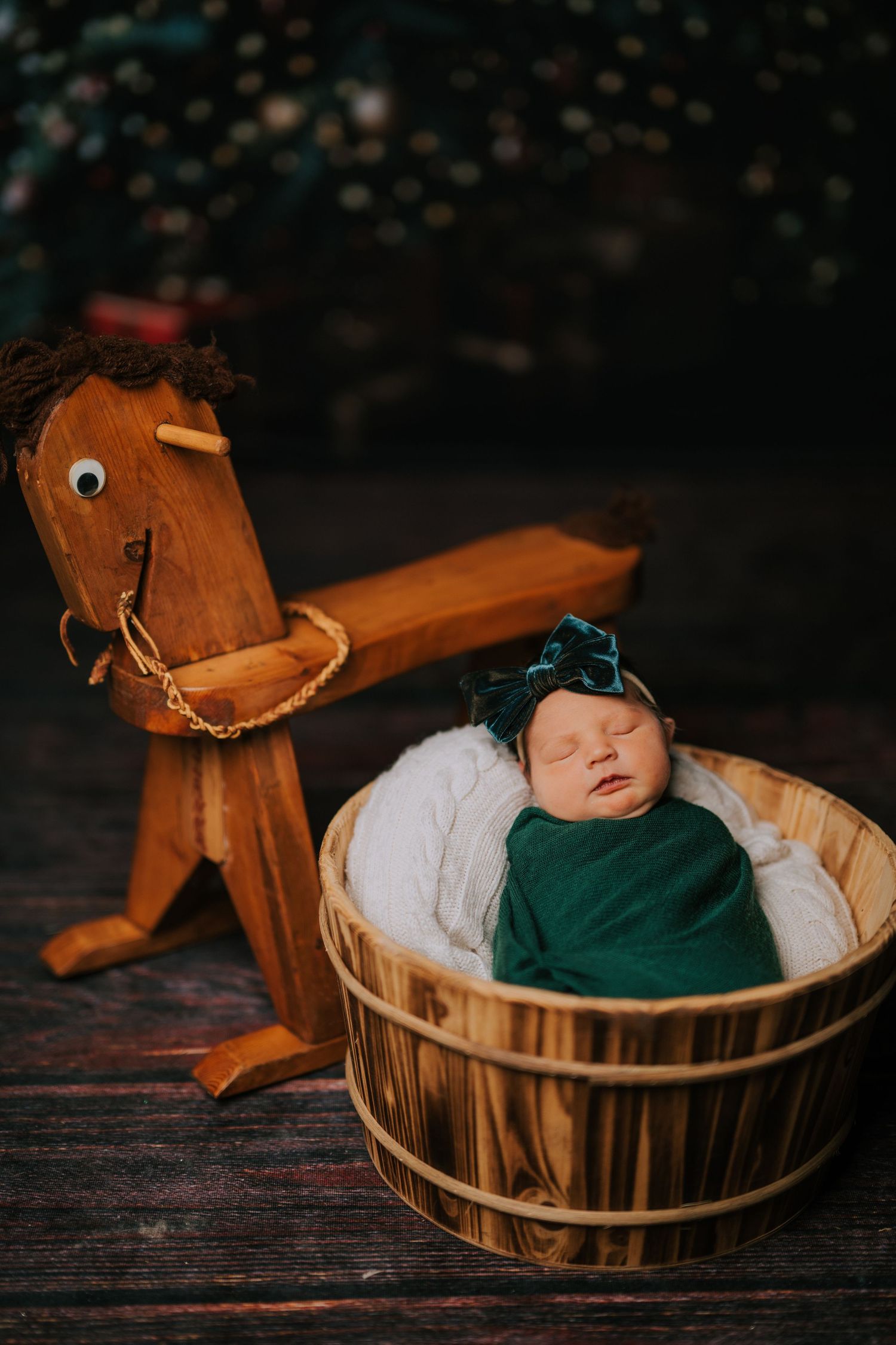 Baby in green outfit sleeping in wooden barrel with decorative horse head.
