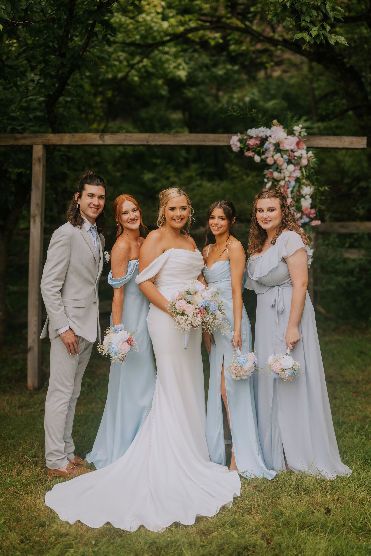 Bridesmaids in powder blue dresses pose with the bride in a white gown outdoors.