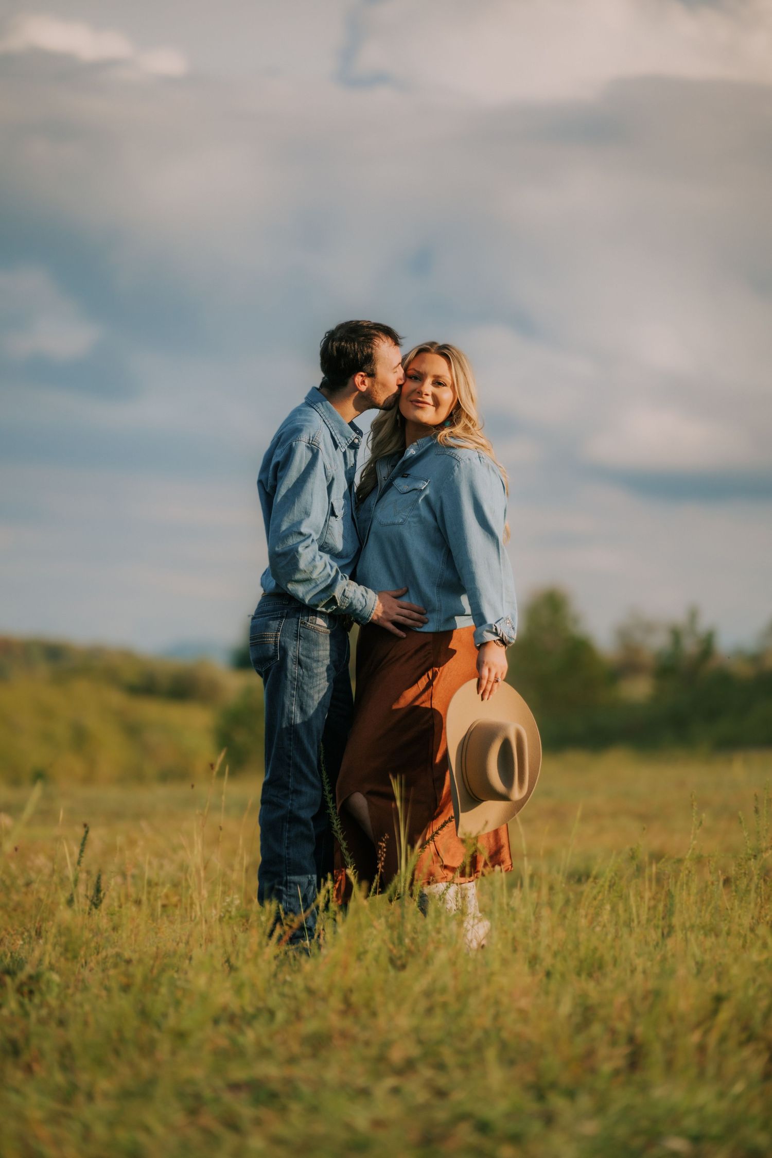 Couple shares intimate moment in grassy field during golden hour wearing casual denim.