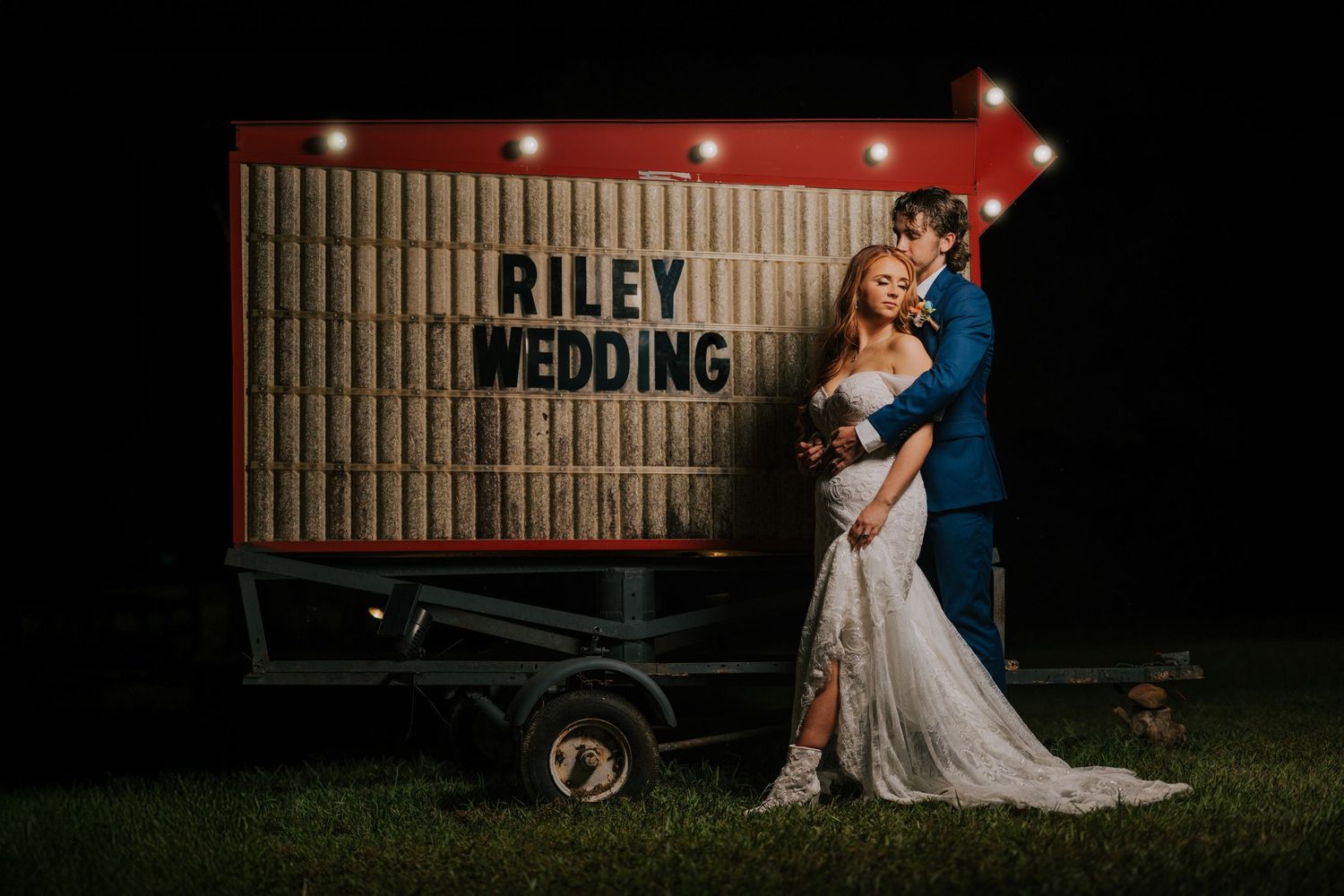 Romantic nighttime wedding photos taken against red barn backdrop with string lights.